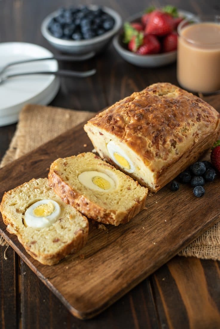 Bacon egg & cheese breakfast loaf cut open so you can see the hard boiled egg on a board served with blueberries, strawberries and coffee