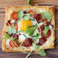 A square of puff pastry topped with cheese, tomatoes, bacon, egg, chives and greens