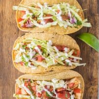3 Baja style fish tacos lined up on a serving board from overhead