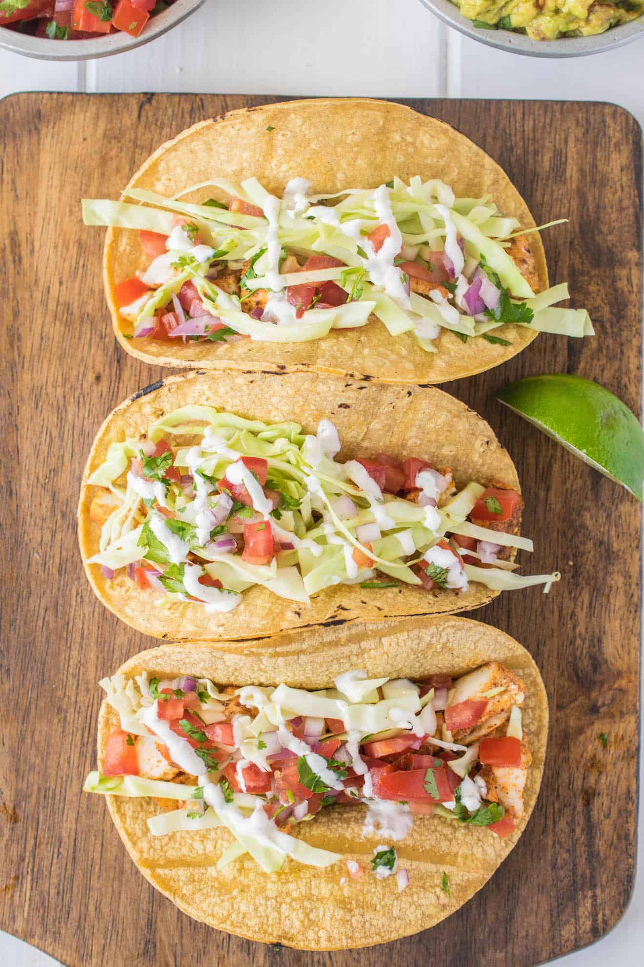3 Baja style fish tacos lined up on a serving board from overhead