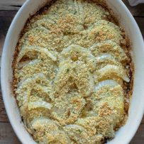 An oval casserole dish with slices of fennel and apple baked with breadcrumbs and parsley