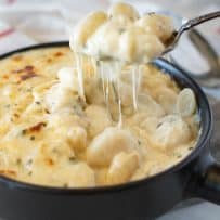 Lifting a spoonful of gnocchi from a cheese sauce with lots of cheese strings