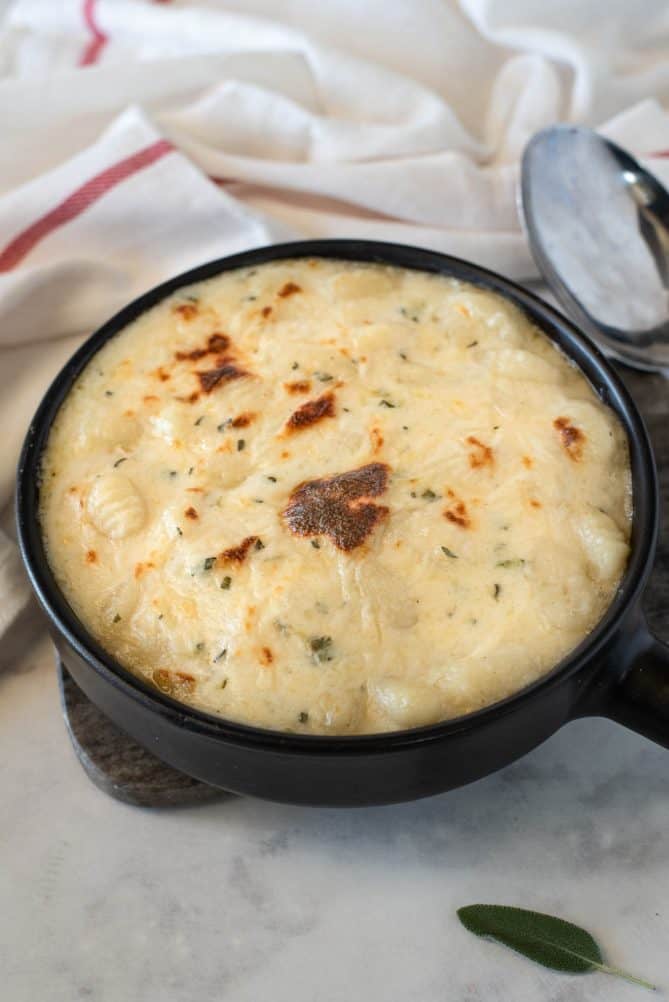 A black round baking dish filled with freshly baked gnocchi in cheese sauce with bubbly brown bits on the top