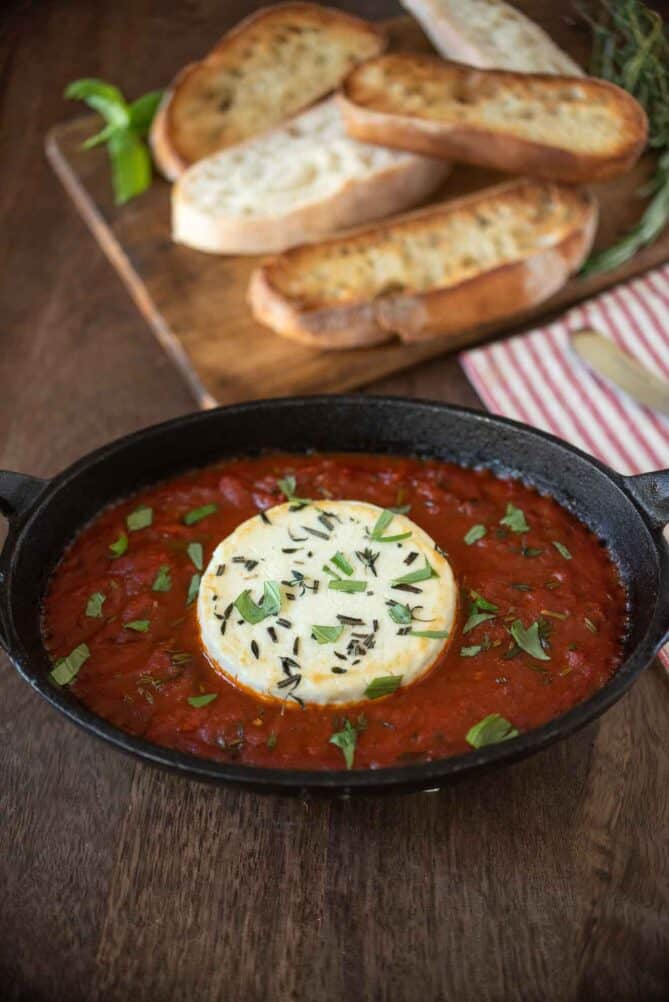 Herb coated goat cheese in a bowl with marinara sauce