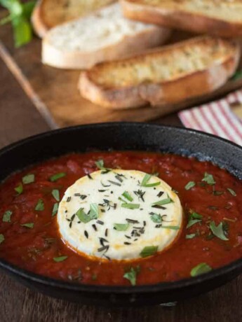 Baked herb goat cheese with marinara sauce in a black oval bowl
