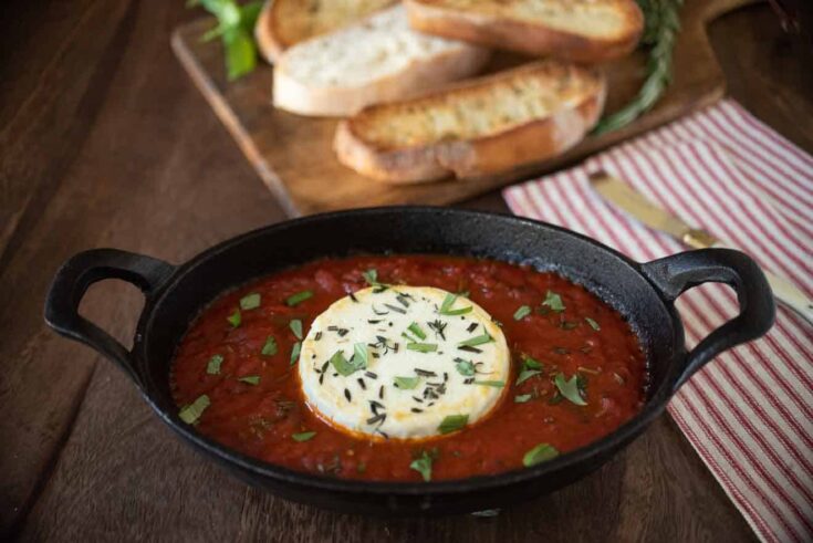 Baked herb goat cheese with marinara sauce in a black oval bowl