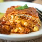 A slice on a white plate showing the layers with salsa and sliced avocado