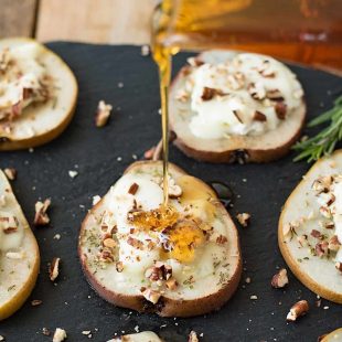 Pouring honey over baked pear slices with goat cheese and chopped pecans