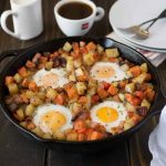 A large cast iron skillet with sweet and white potatoes topped with eggs