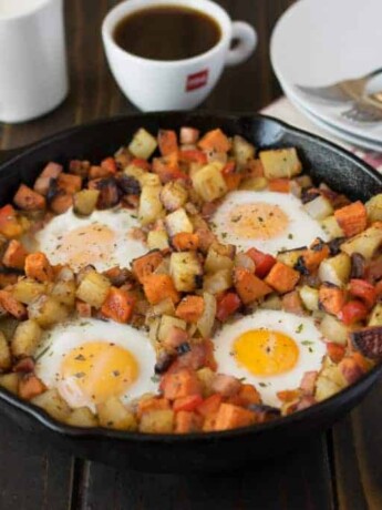 A large cast iron skillet with sweet and white potatoes topped with eggs