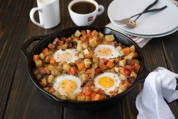 A large cast iron skillet with sweet and white potatoes topped with eggs