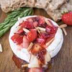 A wheel of brie with melted cheese oozing out topped with strawberries