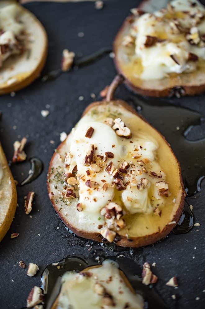 A closeup of a baked pear slice with melted goat cheese, honey and pecans