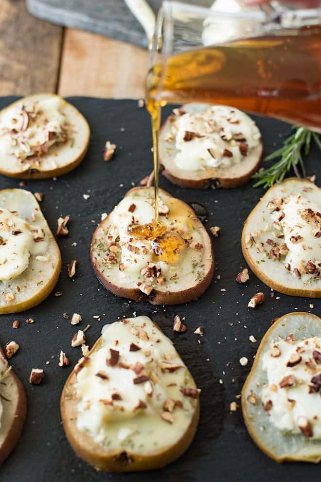 Pear slices on a platter topped with goat cheese, pecans and honey