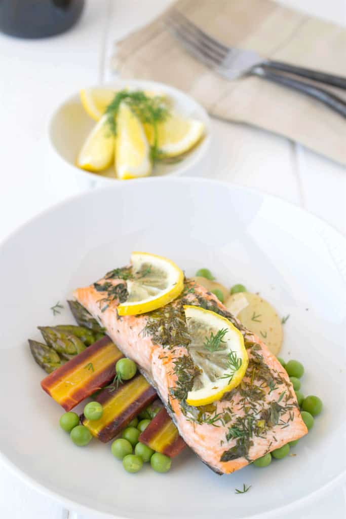  Baked salmon with spring vegetables  served on a white plate with fresh lemon slices