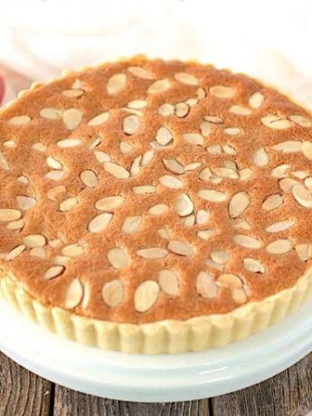 A whole bakewell tart on a cake stand ready to be sliced