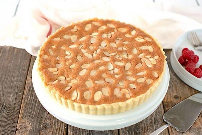 A whole bakewell tart on a cake stand ready to be sliced