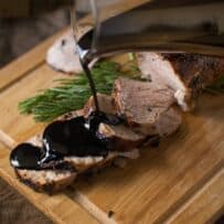 Juicy pork tenderloin slices being drizzled with thick balsamic glaze