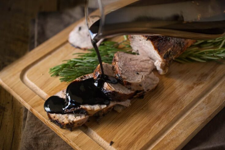 Juicy pork tenderloin slices being drizzled with thick balsamic glaze