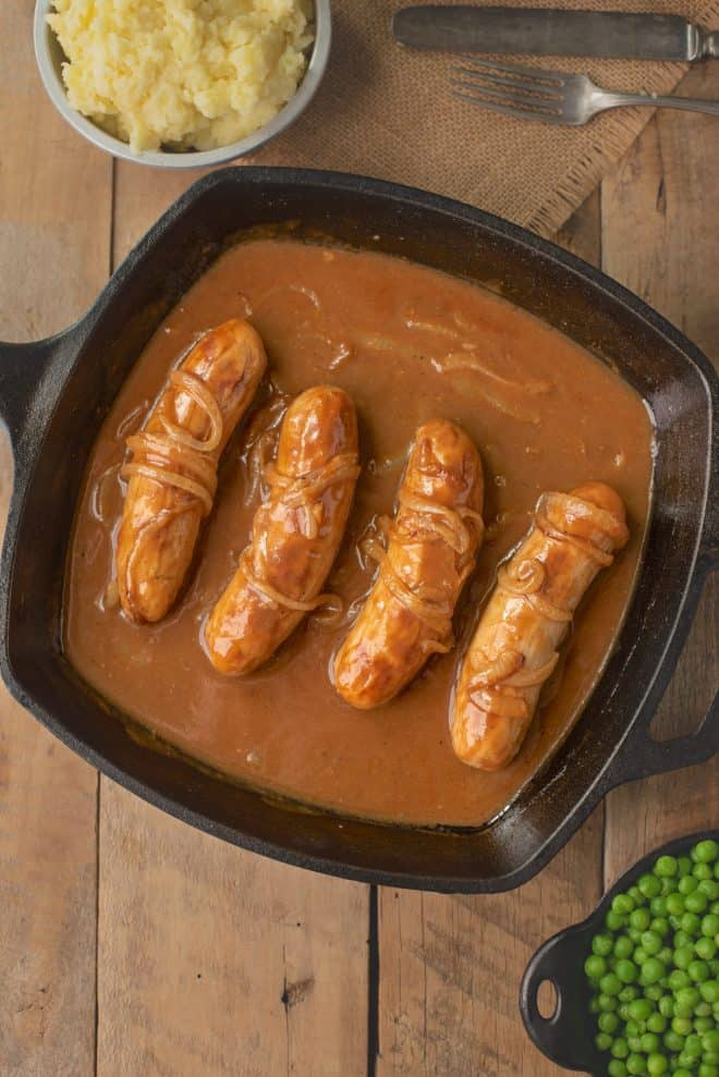 4 British bangers in a cast iron skillet cooking in onion gravy