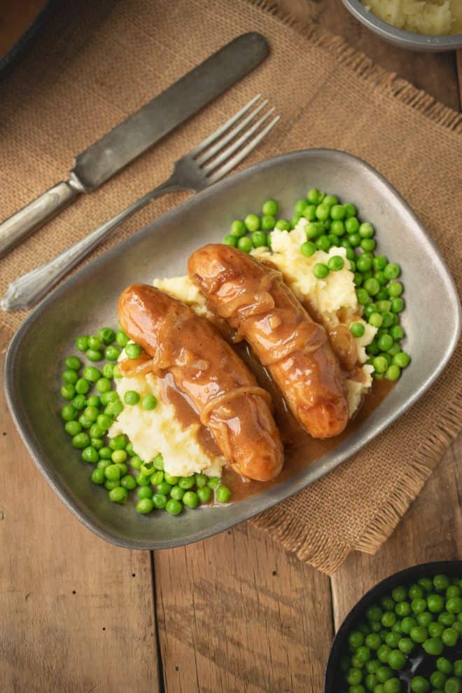 Bangers and mash with onion gravy and peas on a grey plate