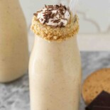 A creamy milkshake in a bottle with a crumb rim and topped with whipped cream