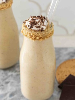 A creamy milkshake in a bottle with a crumb rim and topped with whipped cream