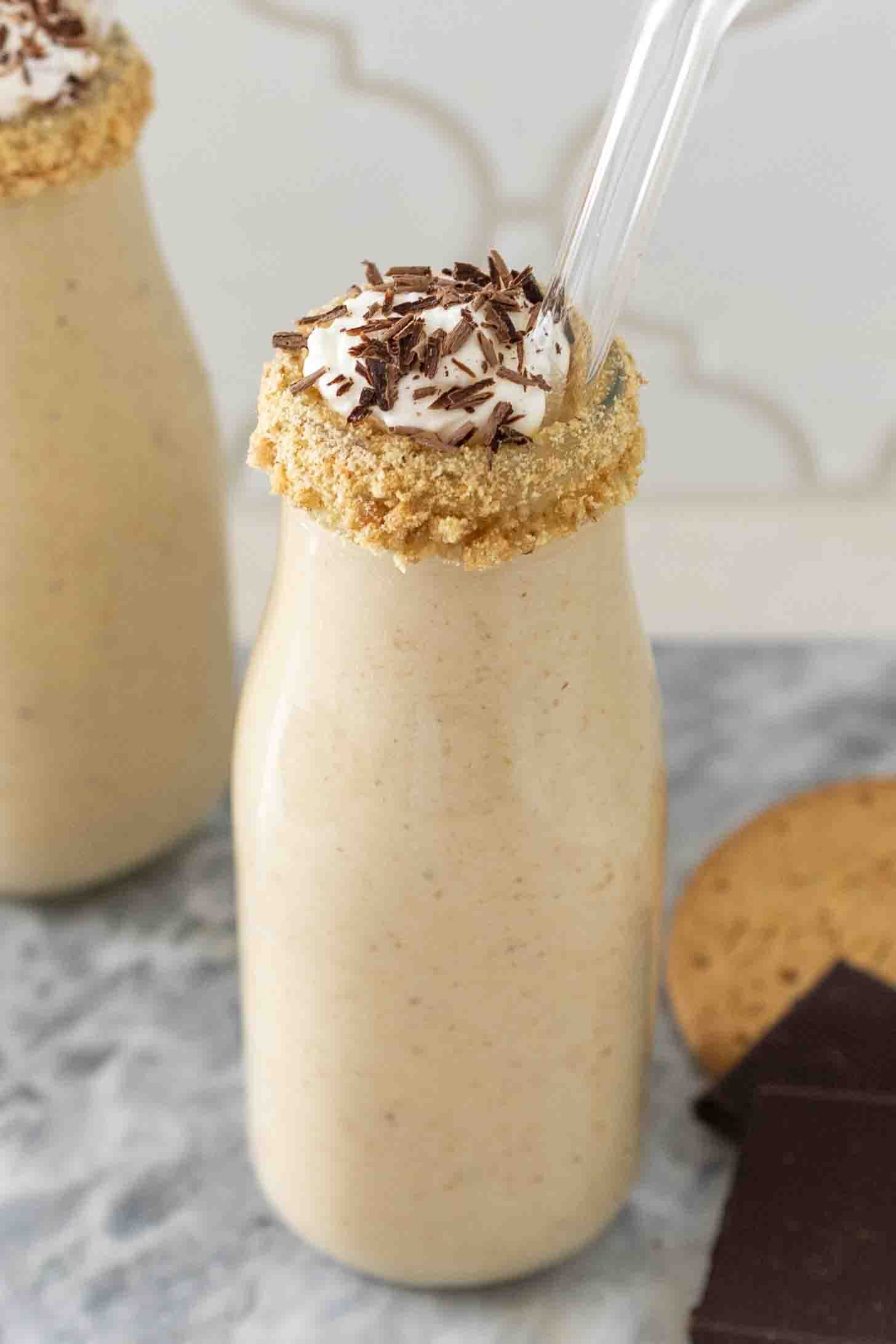 A creamy milkshake in a bottle with a crumb rim and topped with whipped cream