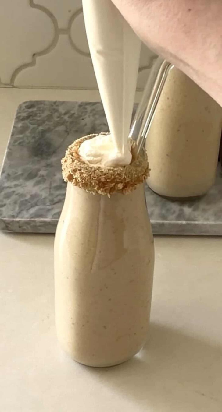 Piping whipped cream on top of a creamy milkshake