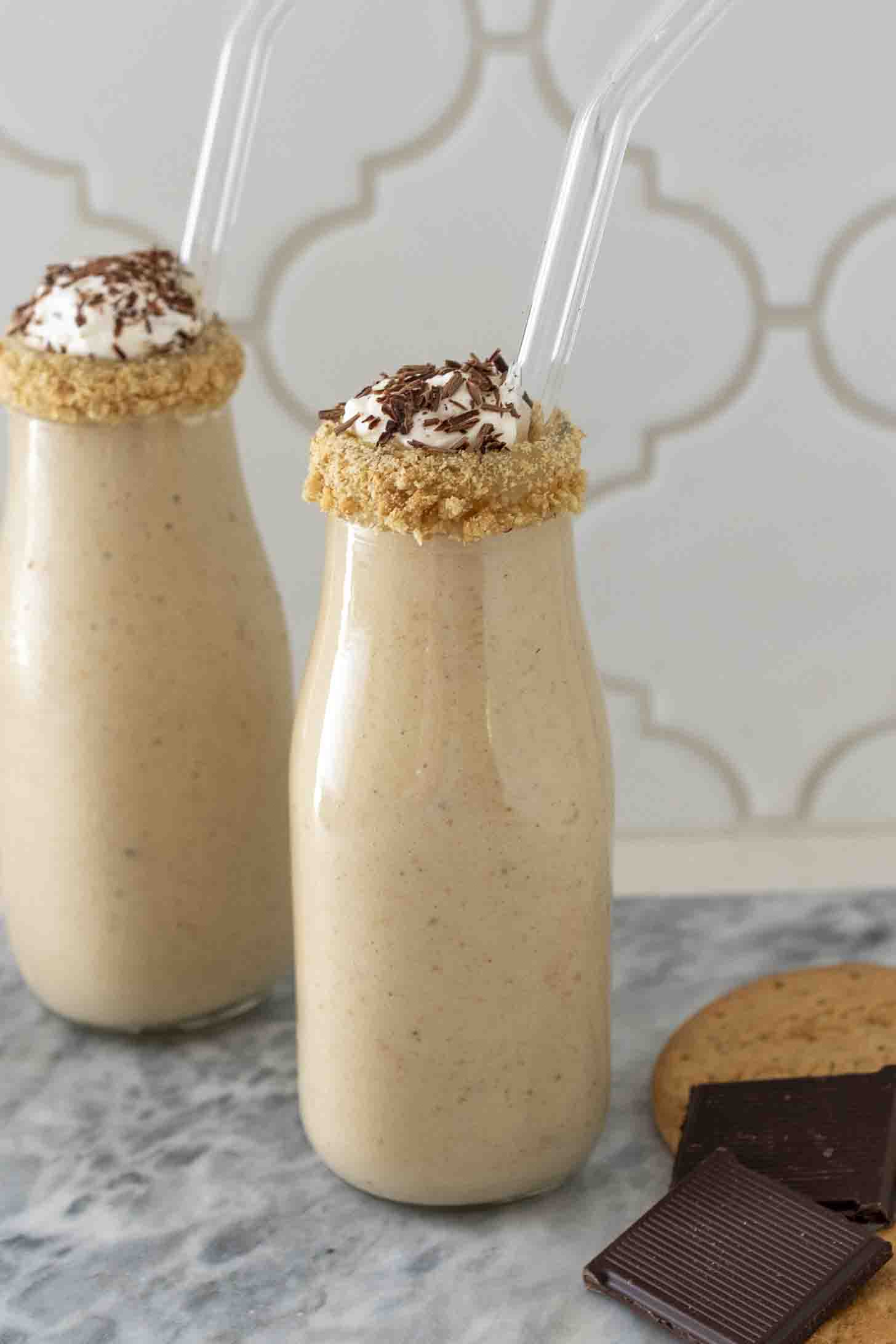 Tall glass of banoffee pie milkshake topped with whipped cream, sliced fresh bananas, crushed graham crackers, and caramel.