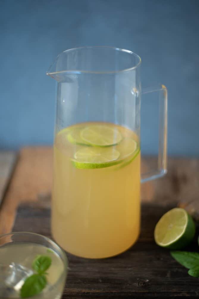 A glass pitcher filled with a herbal tea with lime slices