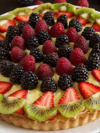 A custard tart decorated with colorful berries and kiwi
