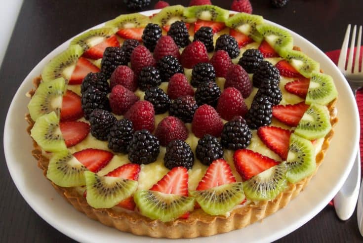 A custard tart decorated with colorful berries and kiwi