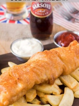 Fish and chips on a board with malt vinegar