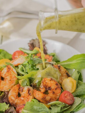 Pouring salad dressing over a shrimp salad