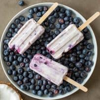 3 popsicles lying down on top of a plate of blueberries