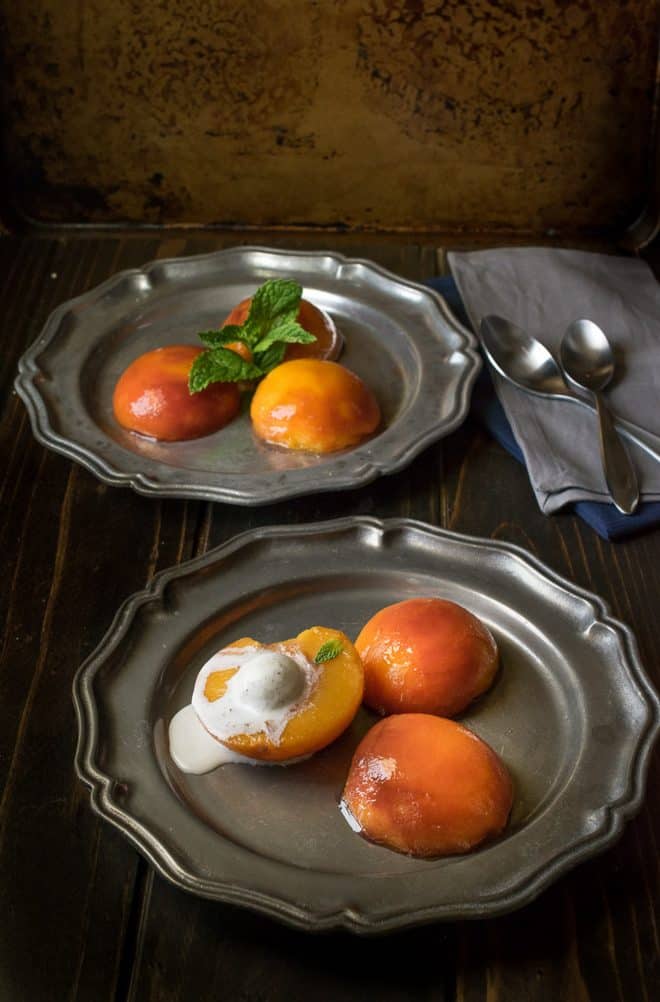 3 poached peach halves on pewter plates one topped with ice cream