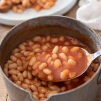 Using a ladle to lift some baked beans from a pan