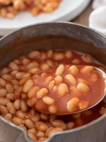 Using a ladle to lift some baked beans from a pan