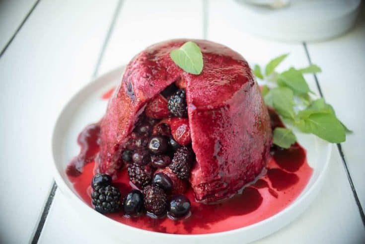 Mixed berries inside a bread pudding covered in colorful berry juice garnished with mint leaves