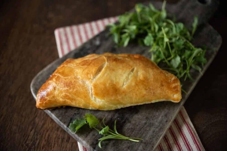 A single cheese and onion pasty on a board with greens