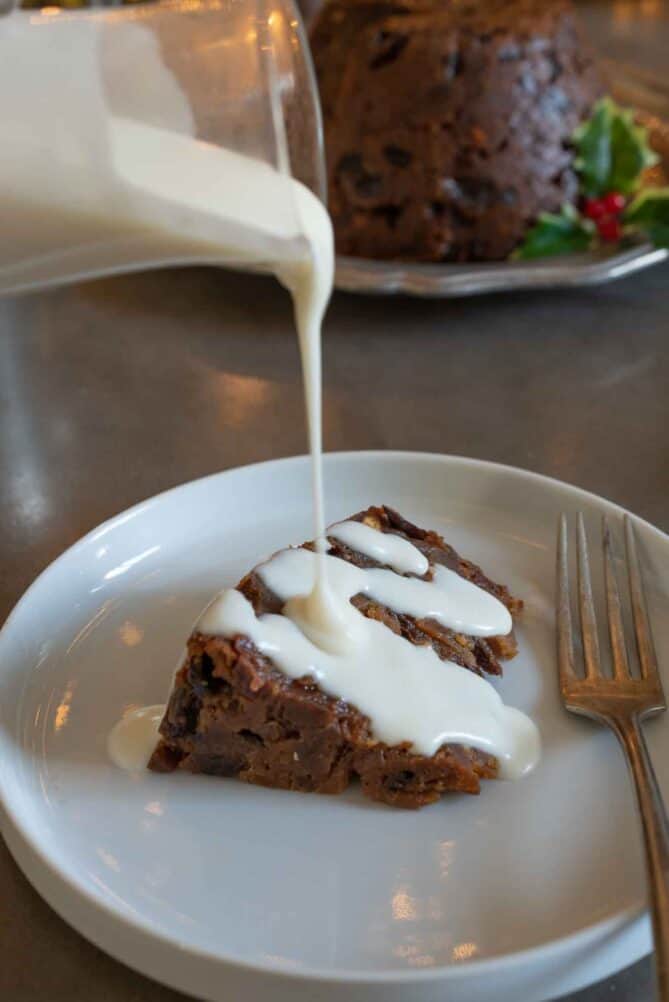 Pouring brandy cream sauce over a slice of Christmas pudding