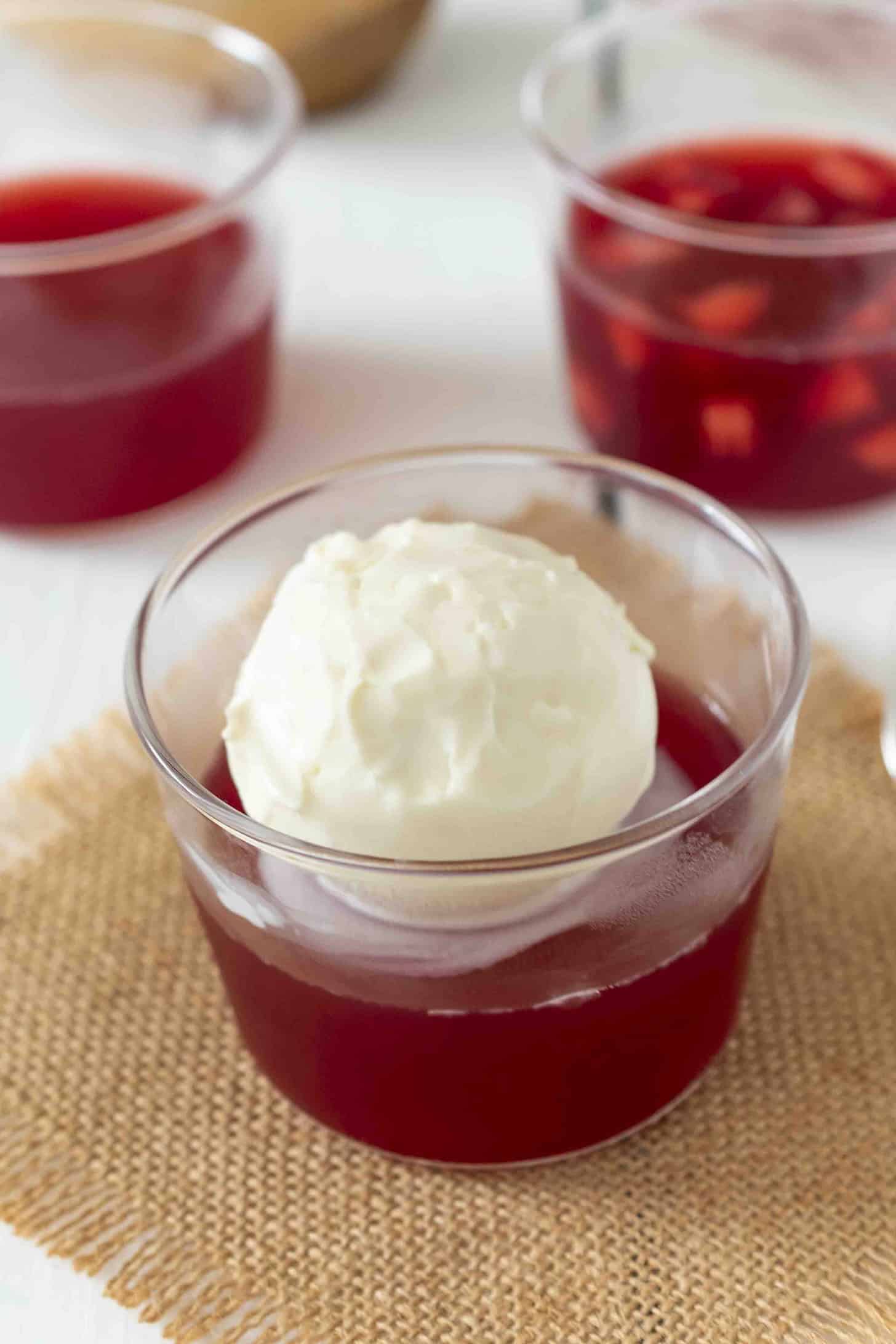 A glass bowl of red jelly/jello topped with a round scoop of vanilla ice cream.