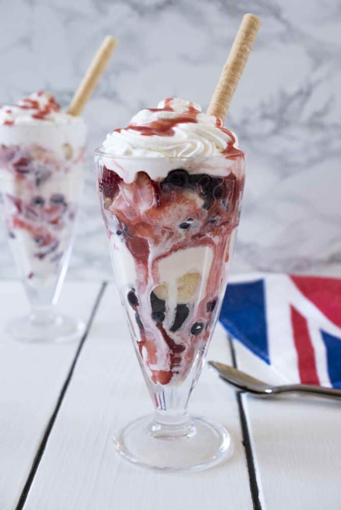 A tall glass filled with fruit ice cream and whipped cream