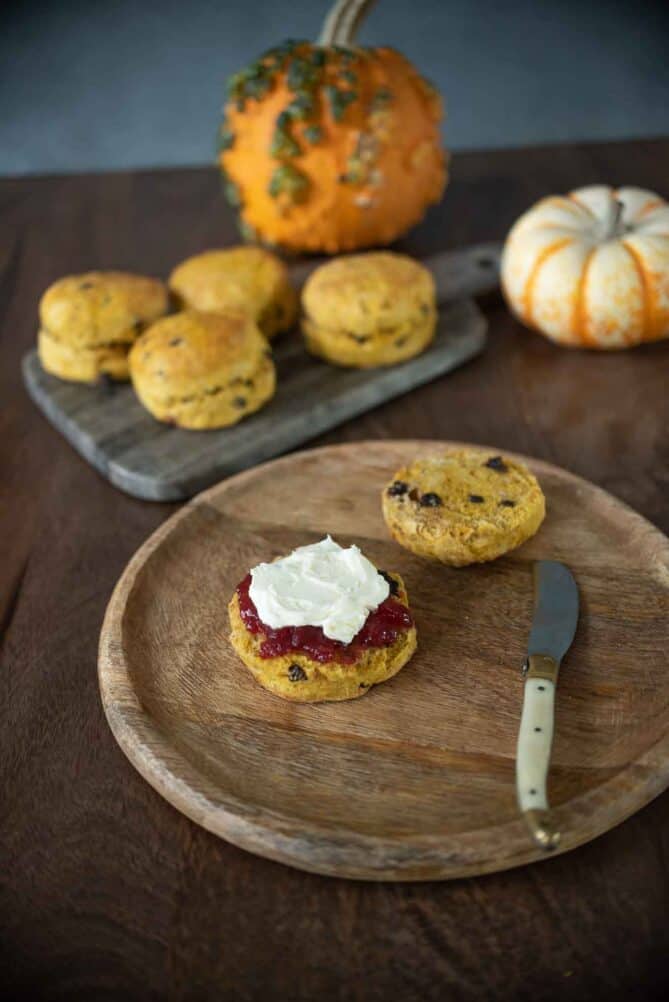 A round wood board with a scone and knife with pumpkins