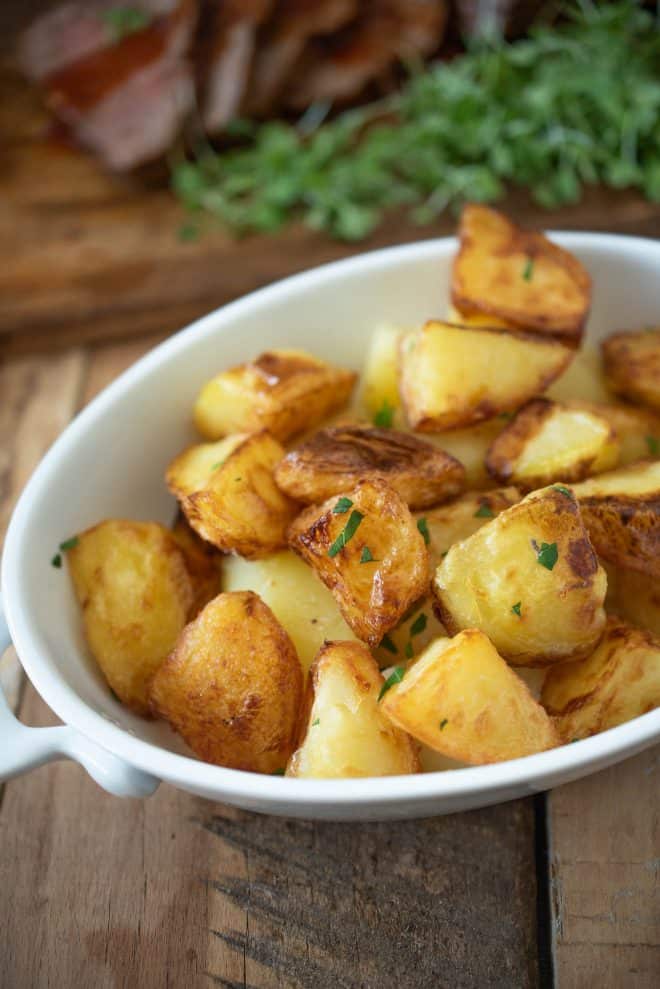 Browned, roasted potatoes in a white oval serving dish