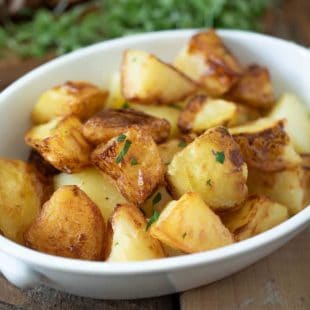 An white oval serving bowl filled with roasted potatoes