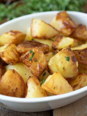 An white oval serving bowl filled with roasted potatoes