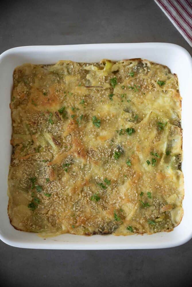 An overhead view of a square, white baking dish filled with cheesy leeks.