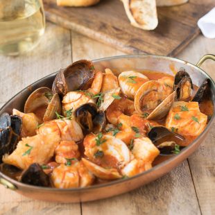 An oval baking dish filled with seafood and shellfish in a tomato broth
